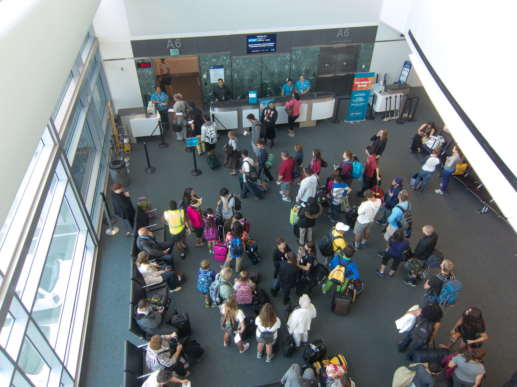 Airport passengers congregating in front of a gatehouse desk and jetbridge entrance.